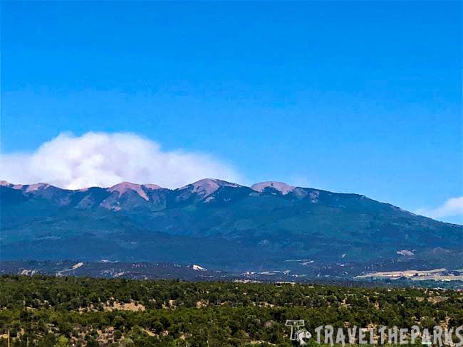 Mountain range with green forests and rocky peaks under a clear blue sky, smoke rises from fire 416 near Mesa Verde National Park