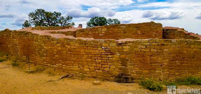 Far View Sites ancient sandstone structure at an archaeological site with trees and a partly cloudy sky.