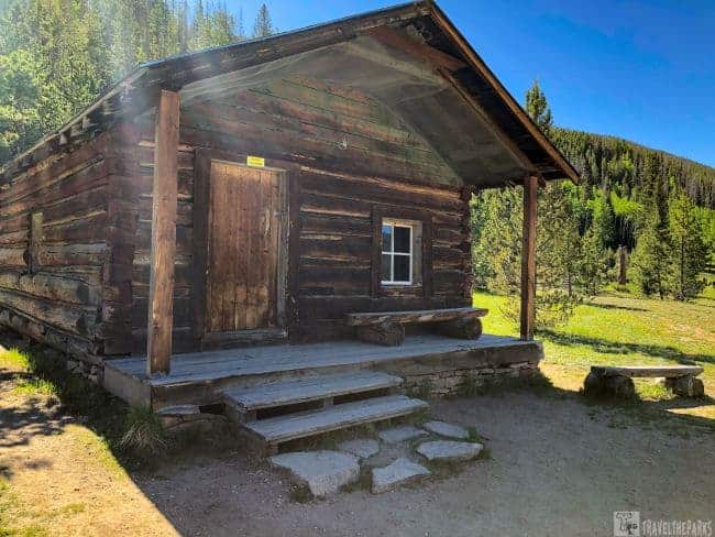 Holzwarth Historic Site a rustic log cabin located in a field, framed by the stunning landscape of Rocky Mountain National Park.
