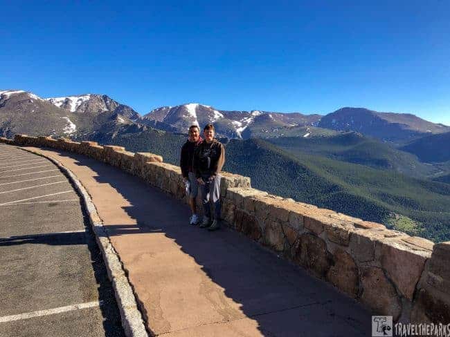 Two individuals stand on a road, gazing at the majestic mountains of Rocky Mountain National Park at Rainbow Curve, Trail Ridge Road.