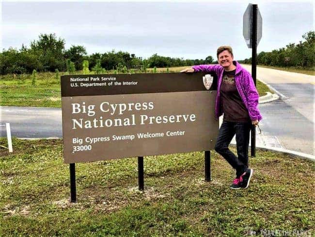 A person standing beside a sign for Big Cypress National Preserve Visitor Center.