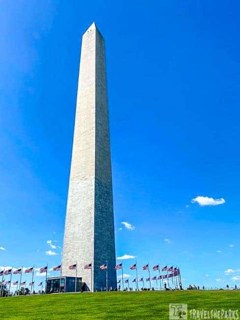 The Washington Monument with American flags at its base against a blue sky.