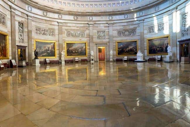 Capitol Rotunda a grand circular room with a polished marble floor, large framed paintings, and white statues against adorned walls.