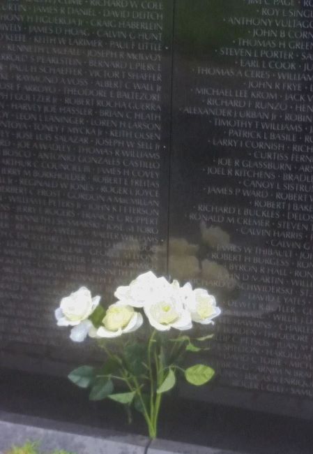 Names on the Vietnanm Wall memorial wall with white roses at the base.