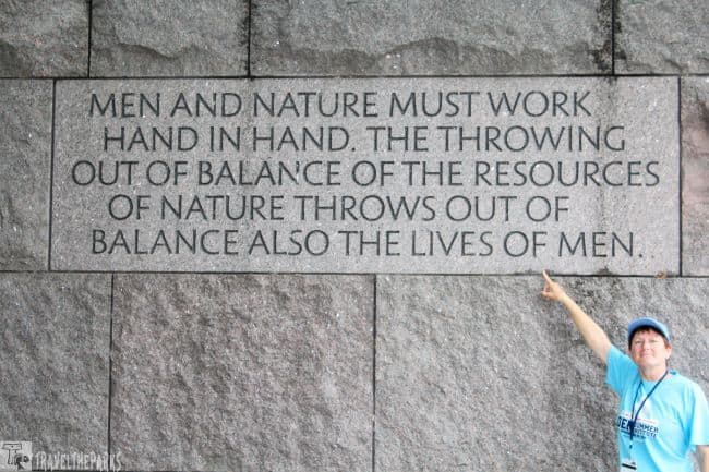 Person pointing to a quote engraved on a stone wall.