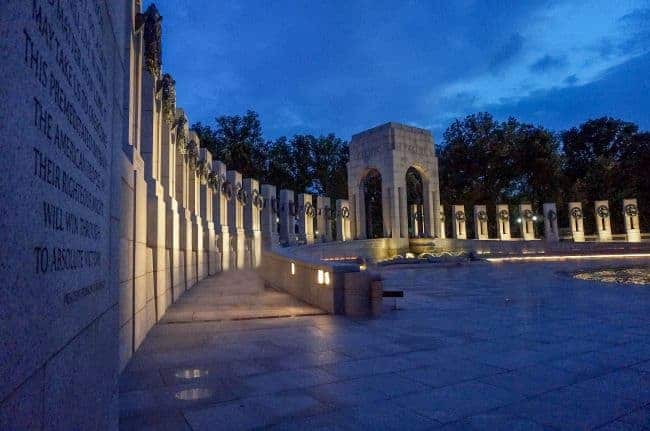 The National World War II Memorial at dusk, with stone pillars and a central illuminated pavilion.