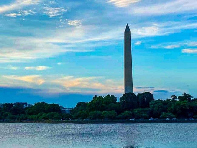 The Washington Monument with a colorful sky and water in the foreground.