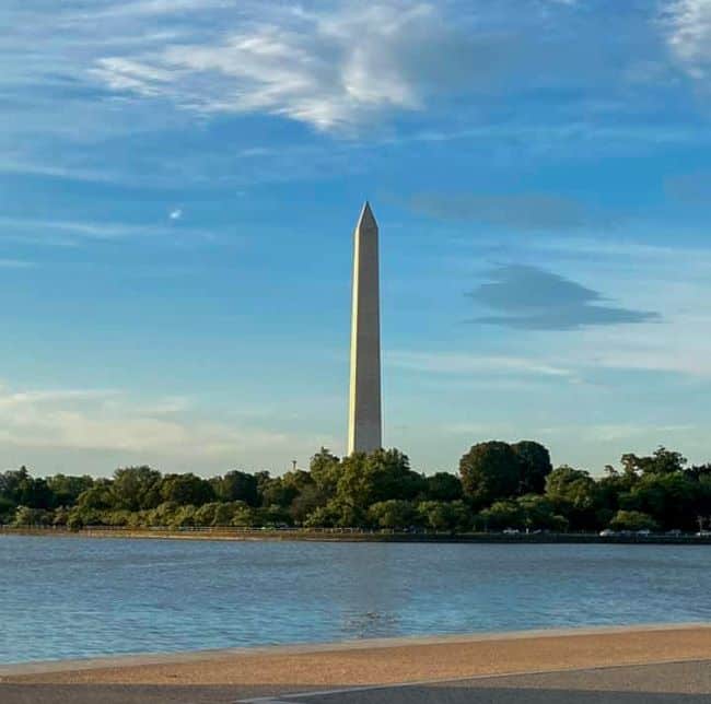 Washington Memorial overlooking the Potomac River-Tall obelisk surrounded by trees with a blue sky and clouds.