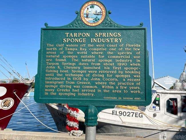 Historical marker highlighting the Tarpon Springs sponge industry, with traditional sponge boats docked in the background—an iconic stop on Sunshine State Orlando Day Trips.
