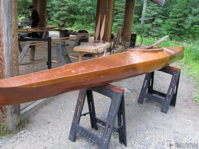 Wooden kayak on sawhorses in an outdoor workshop surrounded by trees at the Alaska Native Cultural Center Village.