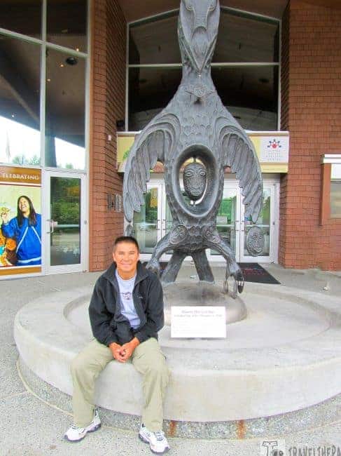 Large sculpture of "Raven the Creator" with a person sitting in front of it at the Alaska Native Heritage Center.
Transcribed Text: Raven the Creator Created by Jim Schoppert, 1998 Property of Alaska Native Heritage Center Collection