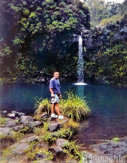 Puohokamoa Falls-Maui: A person standing by a small waterfall and lush greenery.