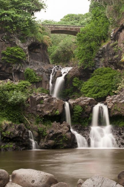Cascading waterfalls at Ohe’o Gulch in Maui with lush greenery and a stone bridge above.