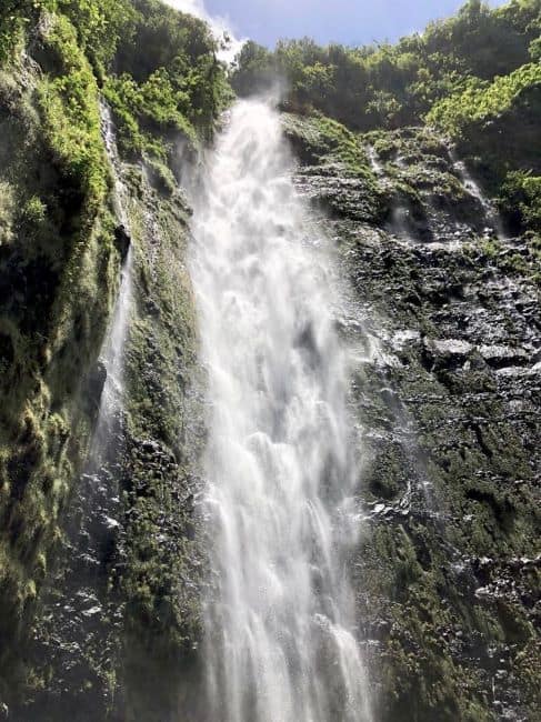Waiamoku Falls: A tall waterfall flows down a rocky cliff surrounded by green vegetation.