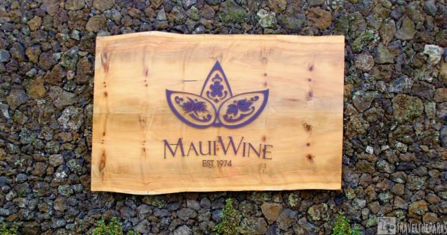 Wooden sign with "MauiWine EST. 1974" on a stone wall.