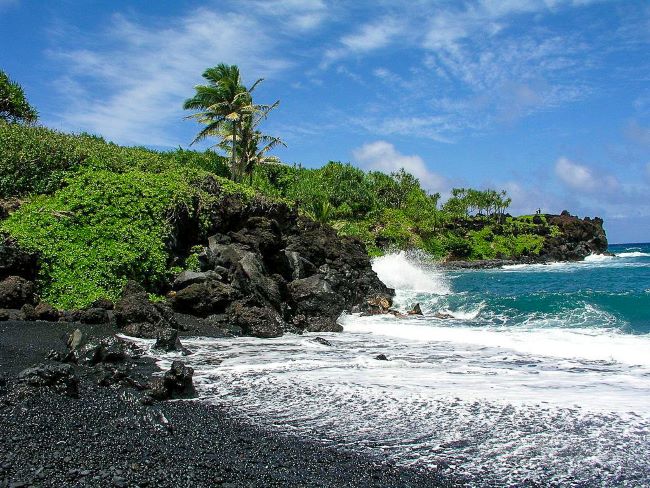 Maui's Waiʻanapanapa State Park: A coastal view with waves crashing over dark rocks, turquoise ocean, and rocky shoreline.