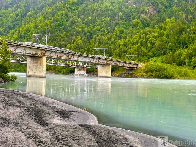 Knik Bridge over a turquoise river with forested hills in the background.