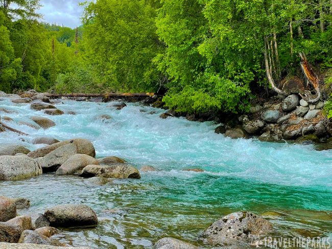 A clear turquoise Susitna river flowing through a forest with lush green trees near Hatcher Pass