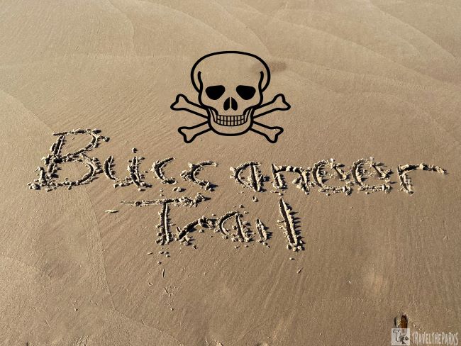 "Buccaneer Trail written in sand with a skull and crossbones above."