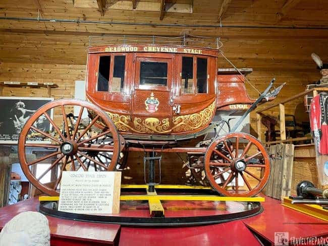 Vintage stagecoach labeled "DEADWOOD CHEYENNE STAGE" with ornate designs on display indoors.
