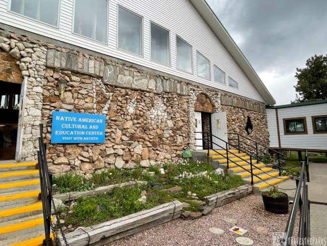 Stone and white-sided building labeled "Native American Cultural and Education Center" with yellow steps and garden.