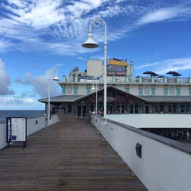 Daytone Beach Pier boardwalk leading to Joe's Crab Shack over the ocean under a blue sky.