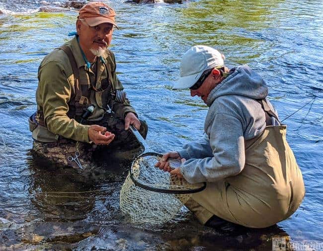 Two people fishing in the Black Hills Rapid Creek, one with a fishing net containing a rainbow Trout.