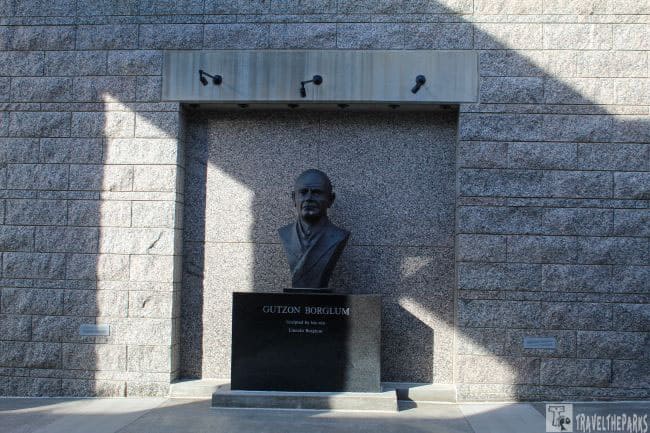 Bronze bust of Gutzon Borglum on a dark pedestal against a stone wall.