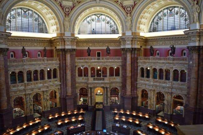 Interior of an ornate library with arched stained glass windows, Corinthian columns, and a semicircular reading area with rows of desks and lamps.