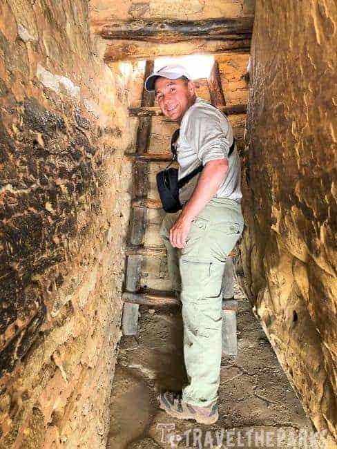 A person climbing a wooden ladder inside a narrow, stone-walled passageway in Balcony House Mesa Verde National Park
