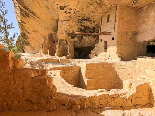 View of ancient stone dwellings and Kiva at Balcony House, Mesa Verde, under a large sandstone cliff.