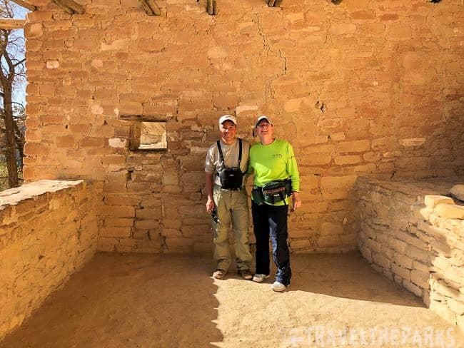 Two people standing inside a stone-walled room with a small window at Balcony House