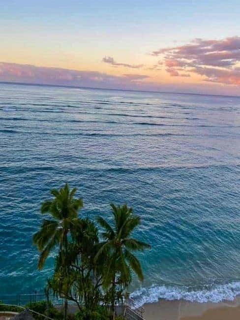 Sunset over a tropical Maui beach with palm trees and gentle ocean waves.

